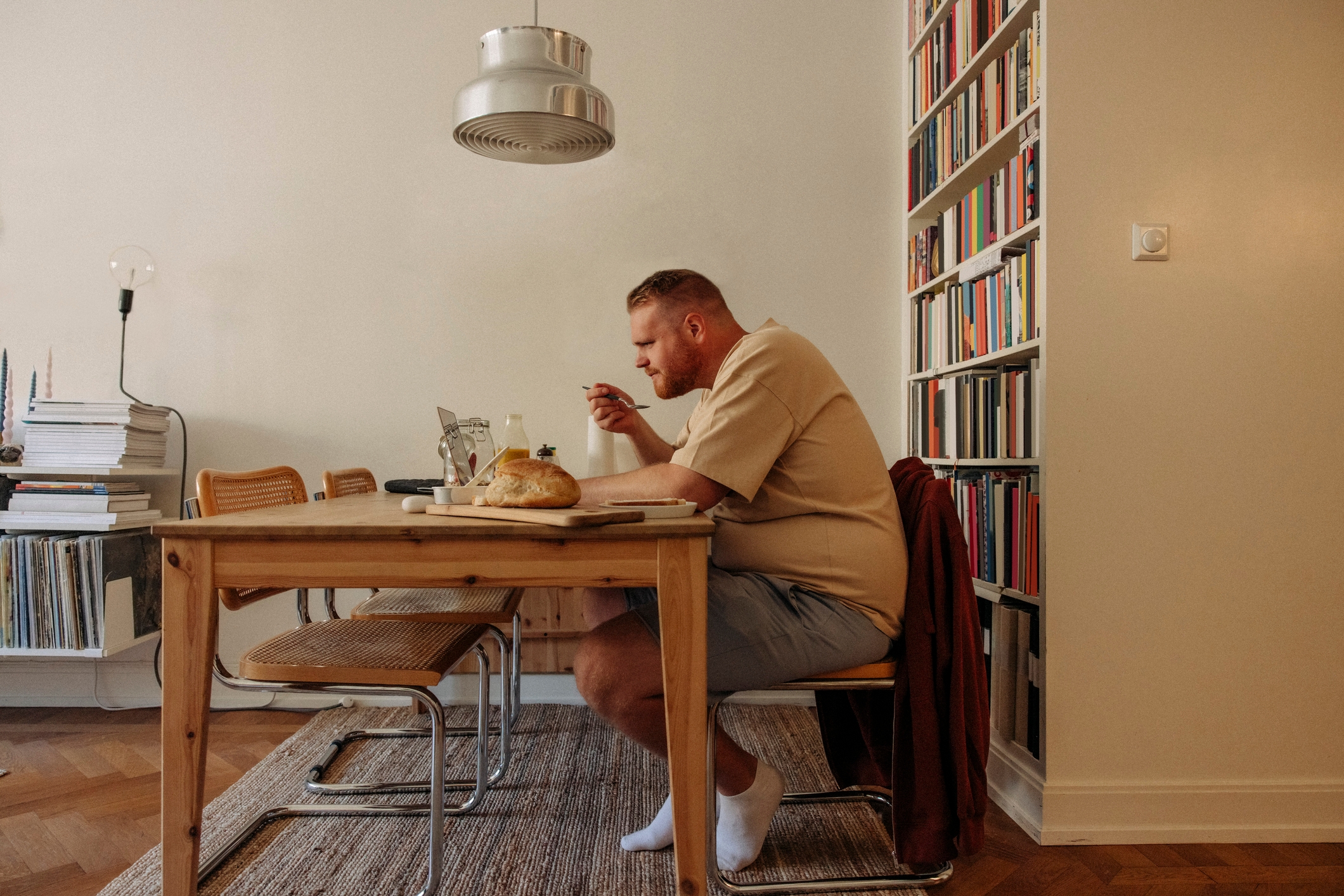 En person sitter ved et spisebord og spiser et måltid, omgitt av bokhyller og et koselig hjemmesetting, og skaper en avslappet og innbydende atmosfære