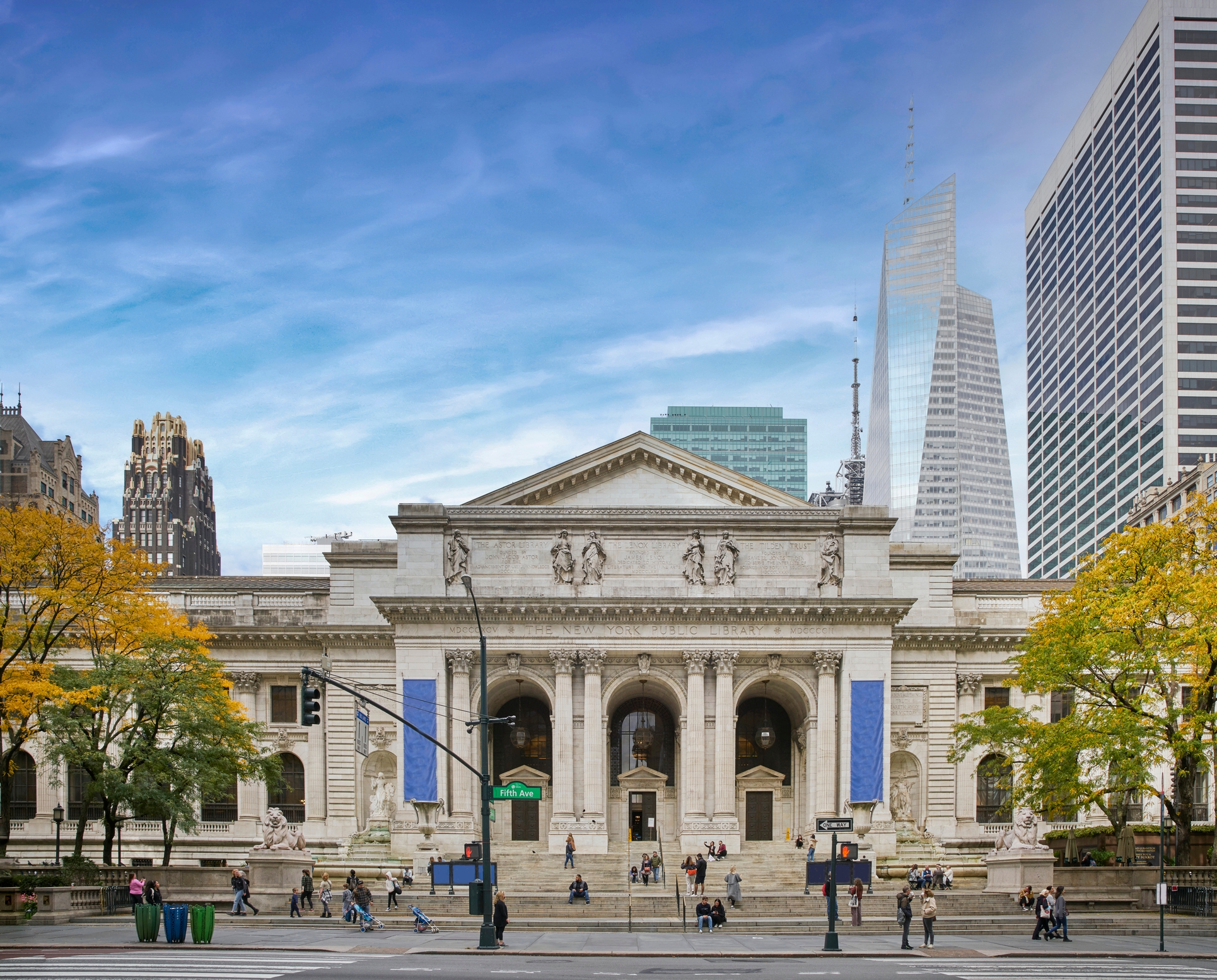 New York Public Library's main entrance with people walking nearby, set against a backdrop of skyscrapers