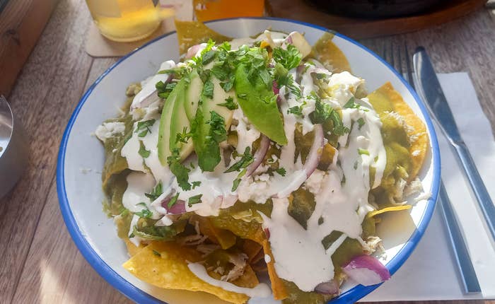 A plate of nachos topped with sliced avocado, cheese, red onions, and drizzled with cream, garnished with chopped herbs