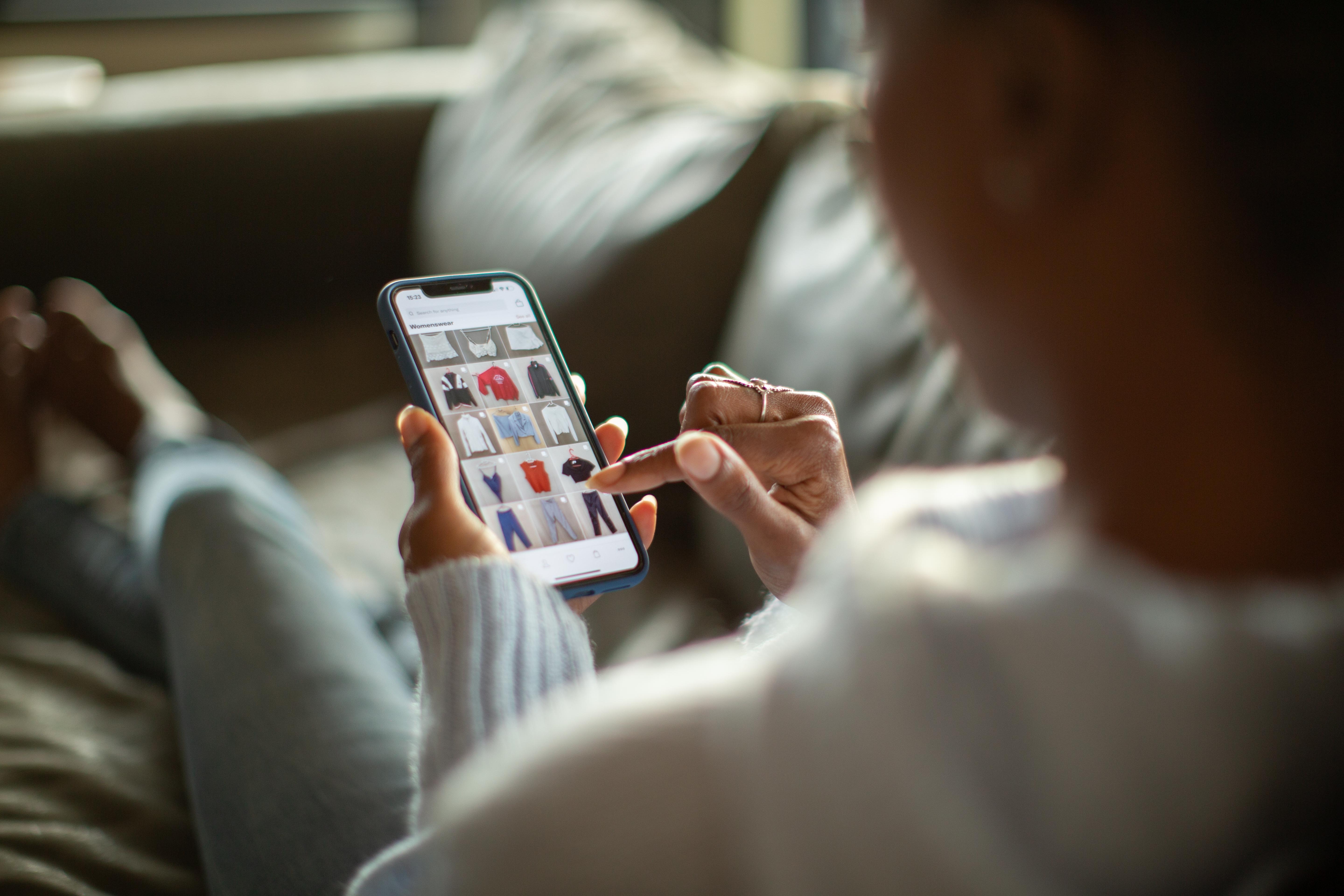 Person som handler etter klær på en smarttelefon mens du slapper av på sofaen