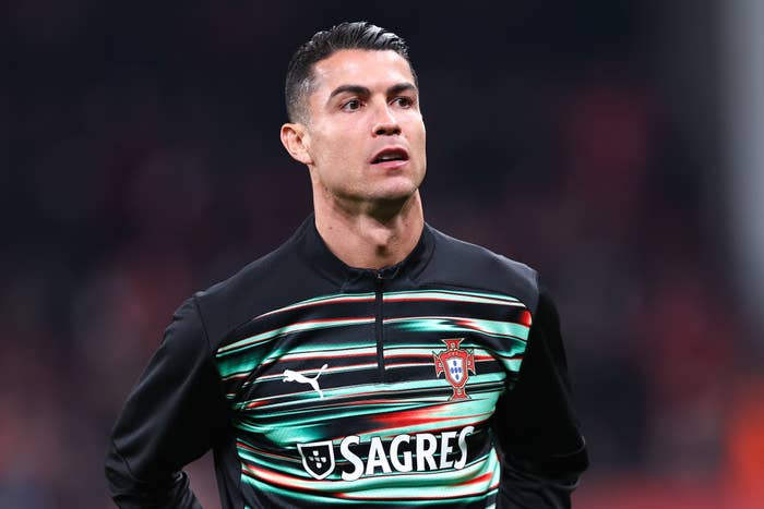 A soccer player stands on the field wearing a jersey with stripes and a team logo, looking focused