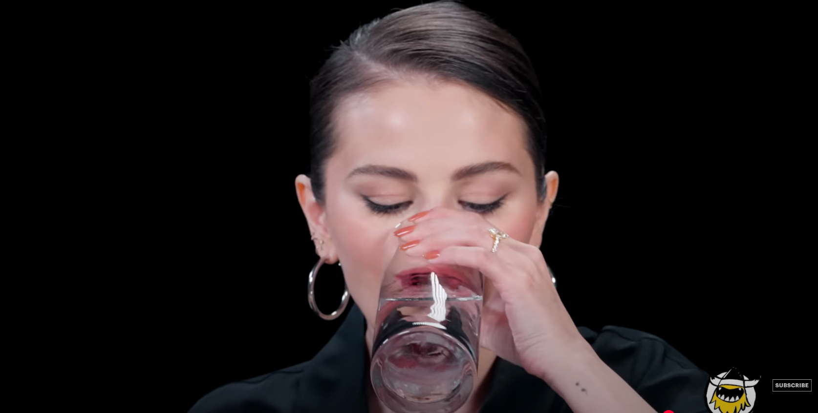 Person drinking water from a glass while wearing hoop earrings and a black outfit