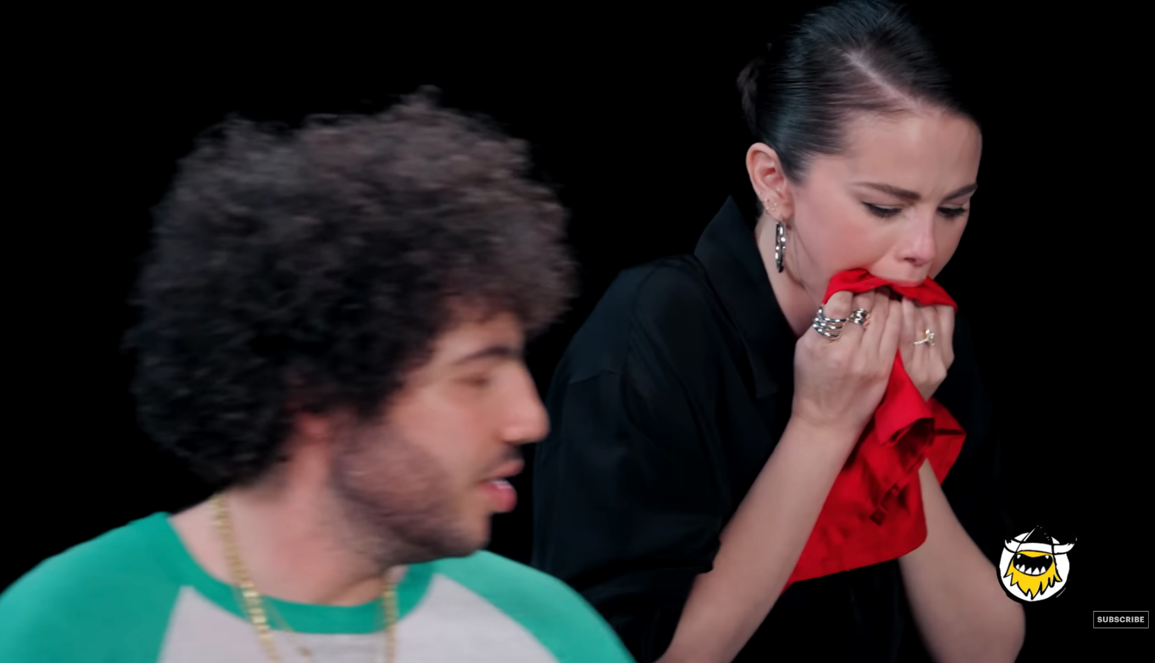 Two people in an interview setting. A woman wipes her mouth with a napkin, looking as if she's reacting to spicy food