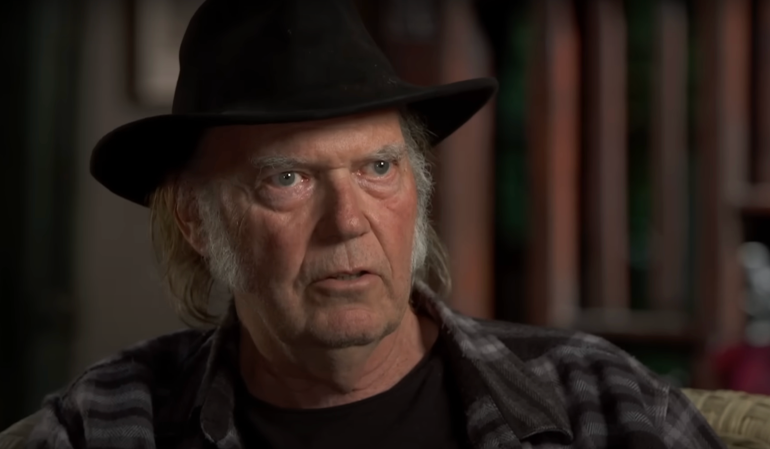 Man in plaid shirt and hat in an interview setting, with a serious expression