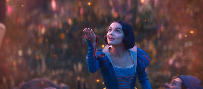 A person in a medieval-style dress looks upward with a joyful expression, surrounded by softly glowing lights