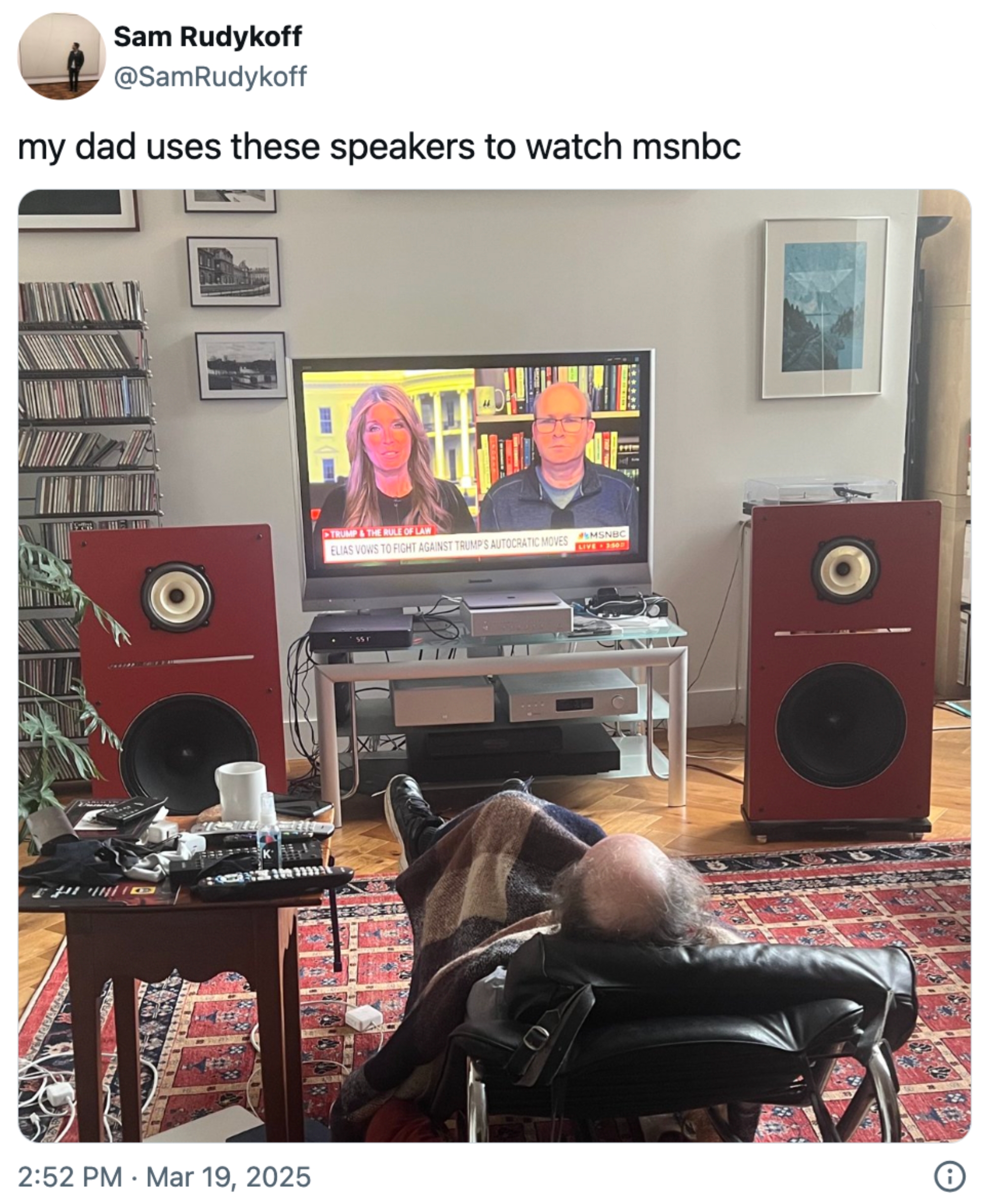 En person ligger i en stol som ser på MSNBC på TV med store høyttalere ved siden av skjermen. Tweet ovenfor sier, & quot; min far bruker disse foredragsholderne for å se MSNBC & quot;