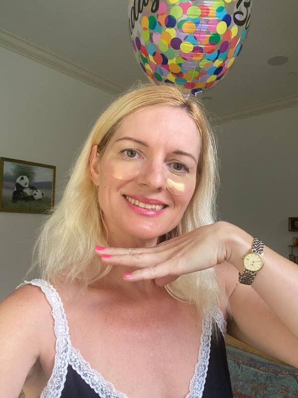 Person smiling indoors, holding a helium balloon with colorful dots. Wearing a laced dress and a wristwatch