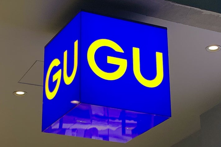 A cube-shaped sign with &ldquo;GU&rdquo; printed in large yellow letters, seen hanging indoors