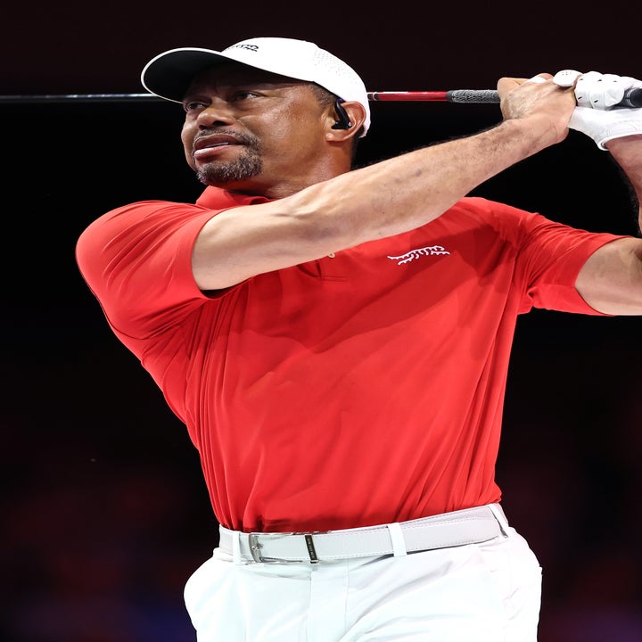 A golfer in a red polo and white cap finishes a swing on a course, focusing intently on the game