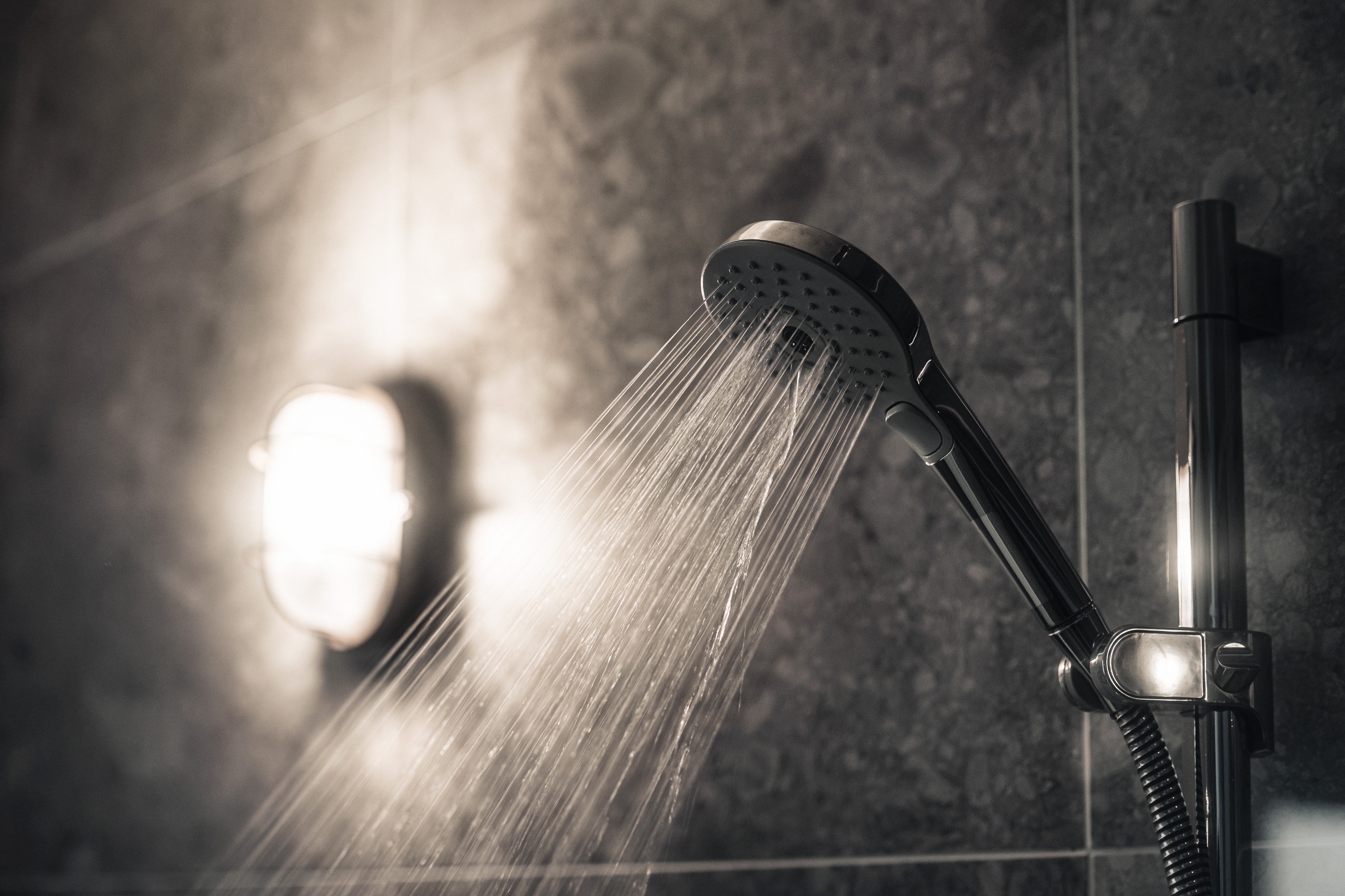 Showerhead spraying water in a dimly lit bathroom with a wall light illuminating the scene