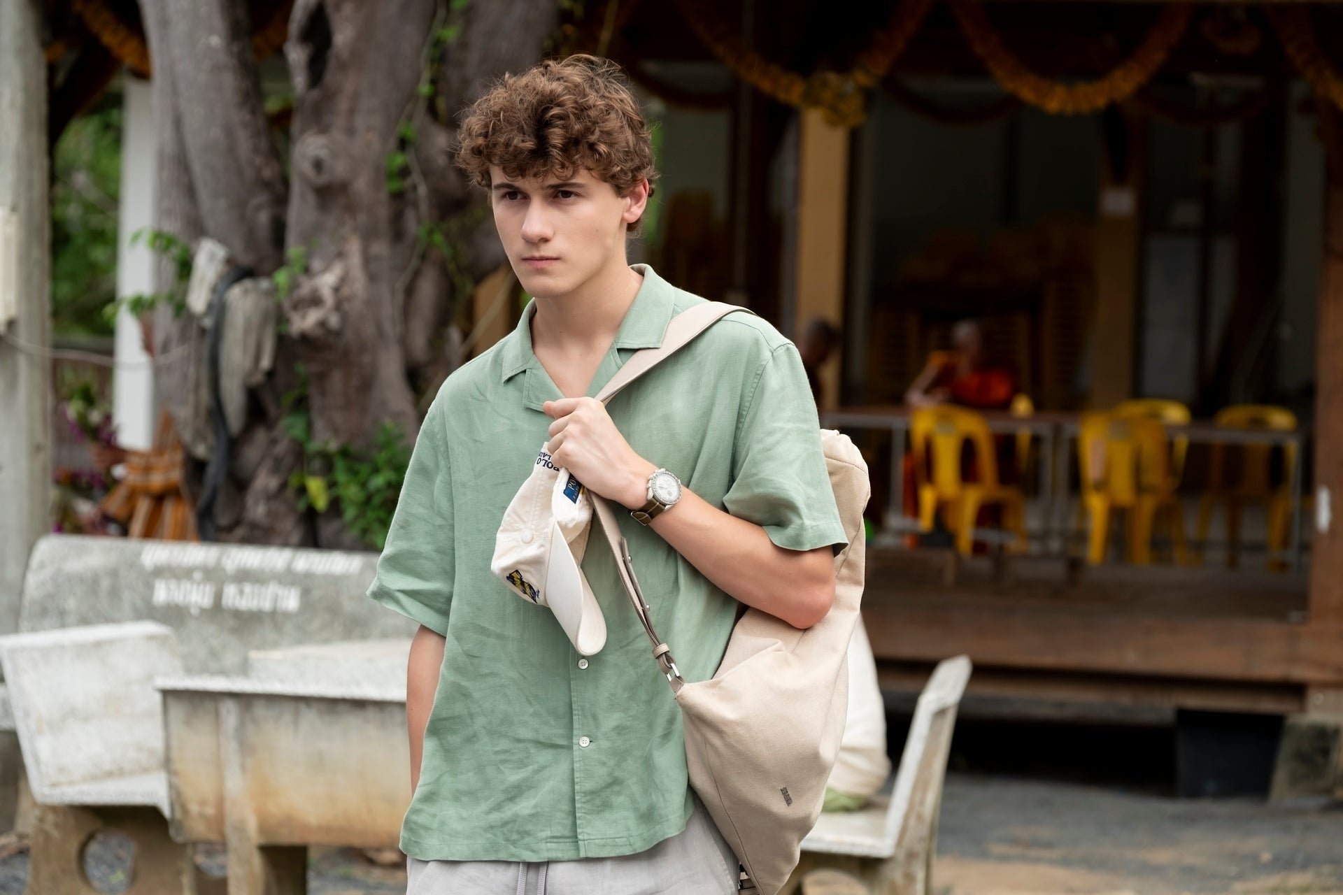 Sam Nivola outdoors wearing a casual short-sleeve shirt, holding a tote bag, with a relaxed expression