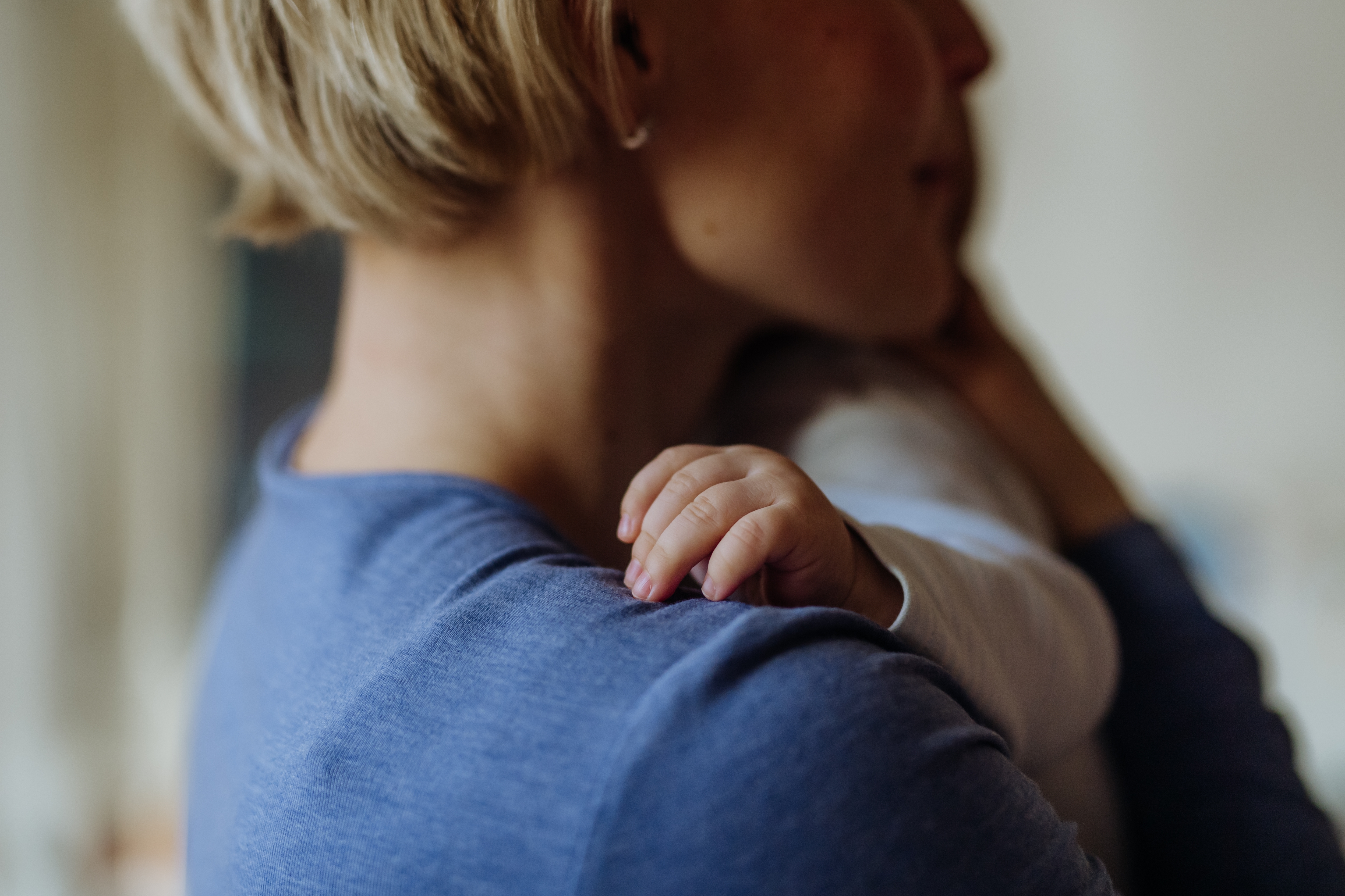 Personen som holder en baby nøye, med babyens hånd som hviler forsiktig på personens skulder, og formidler en følelse av omsorg og kjærlighet