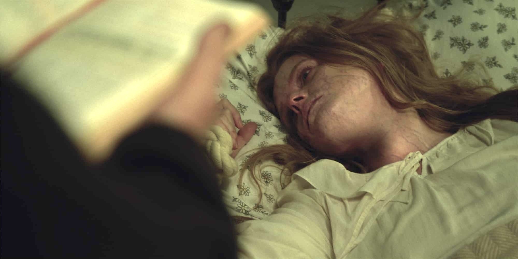 A woman lies on a bed looking distressed, while a figure holds an open book in the foreground, suggesting a tense or supernatural scene