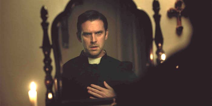 Person in clerical attire looks intensely in a mirror with candles and a cross in the background, suggesting a dramatic scene