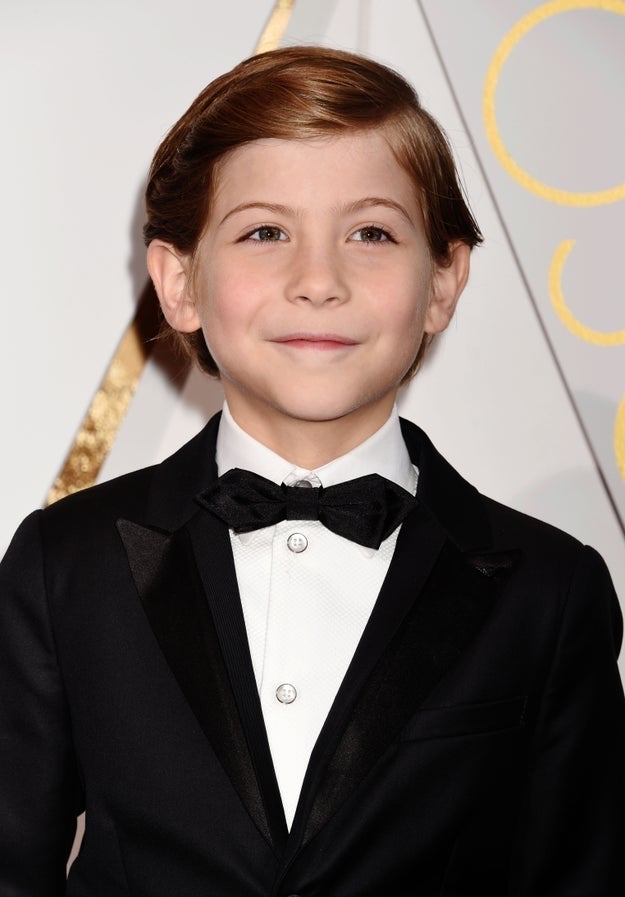 Young child wearing a formal black tuxedo with a bow tie on a formal event backdrop