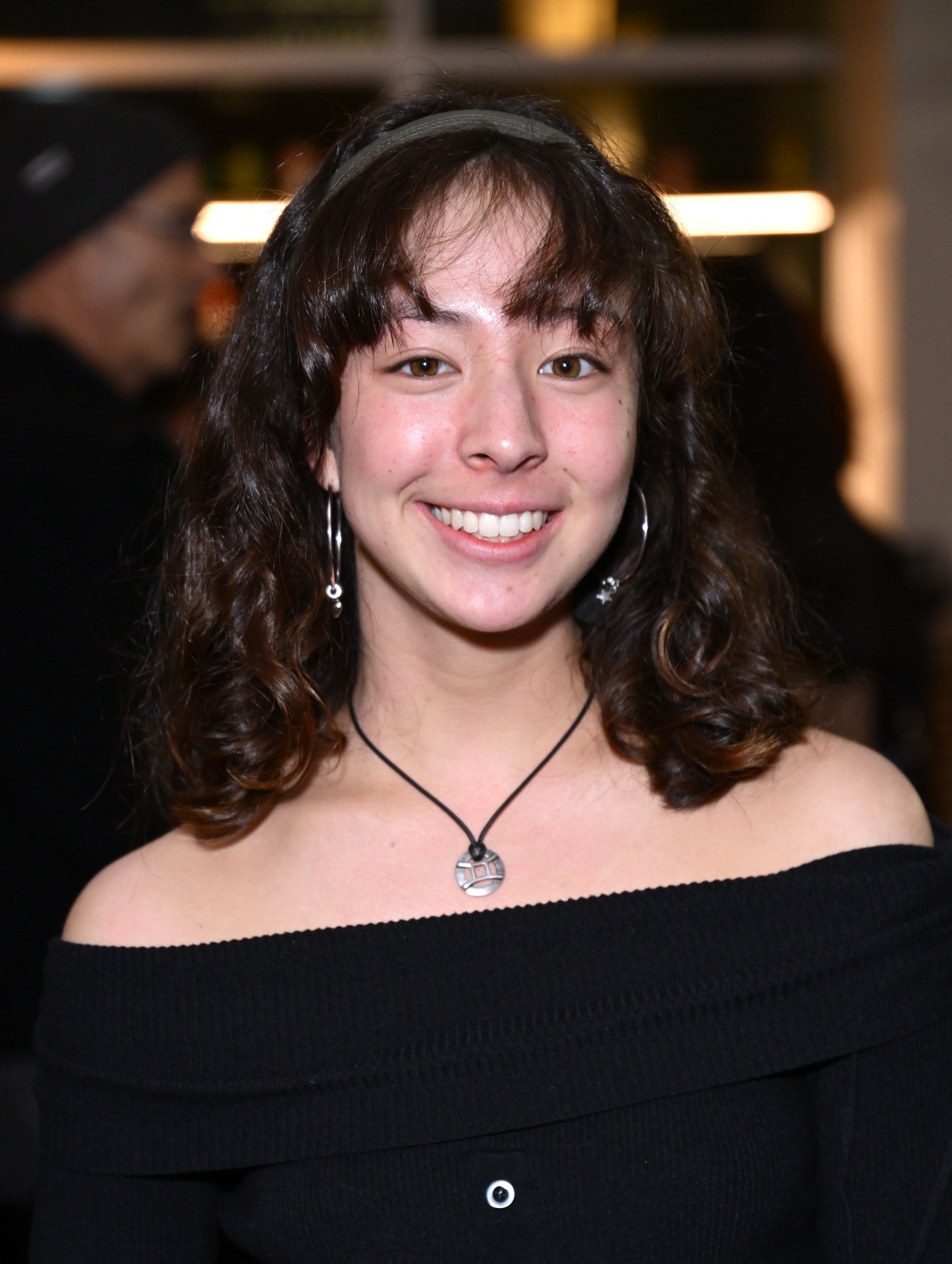 Person smiling, wearing an off-the-shoulder top and dangling earrings, in a casual setting