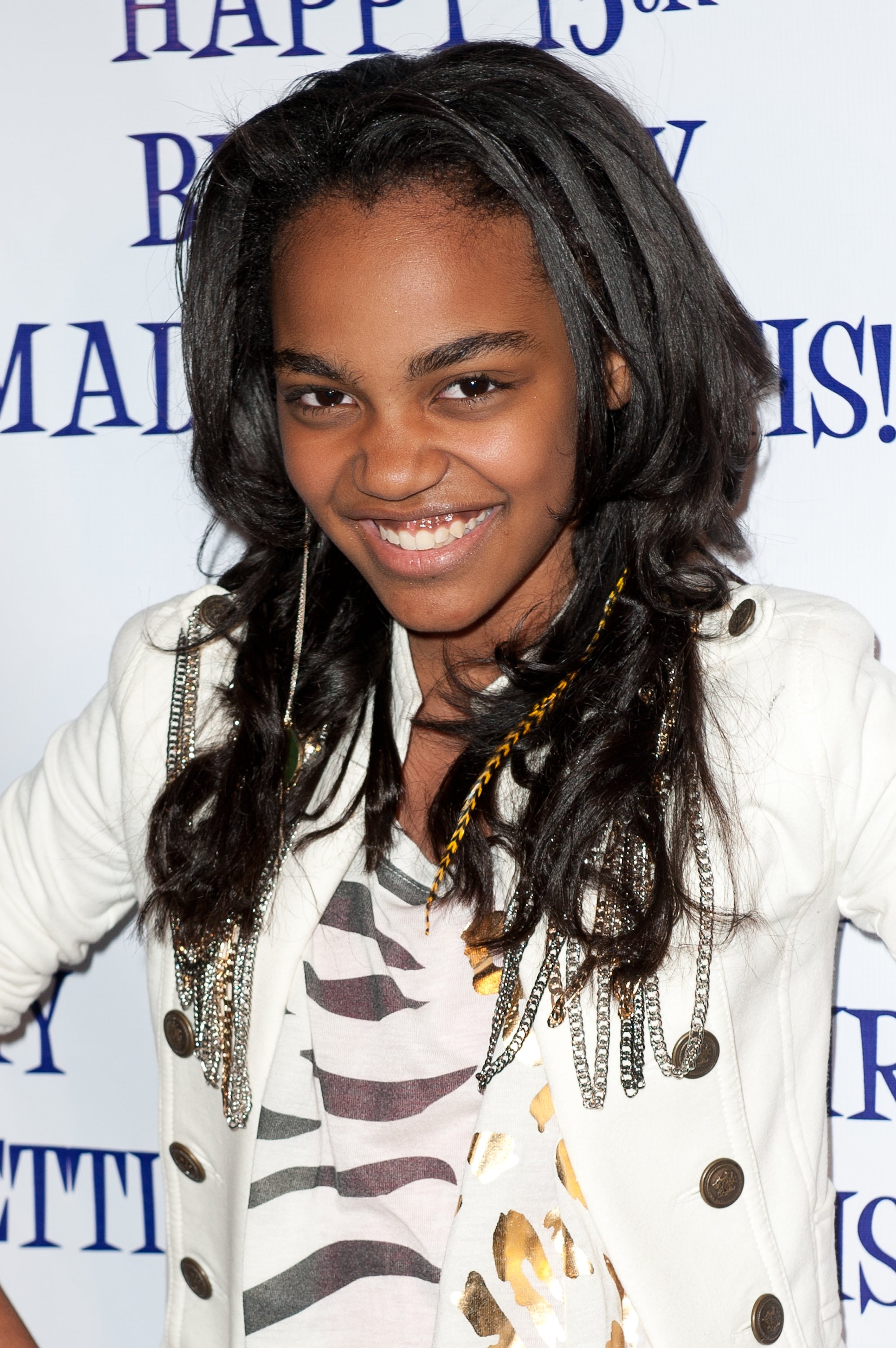 Young person smiles at an event wearing a stylish jacket with embellishments over a patterned top