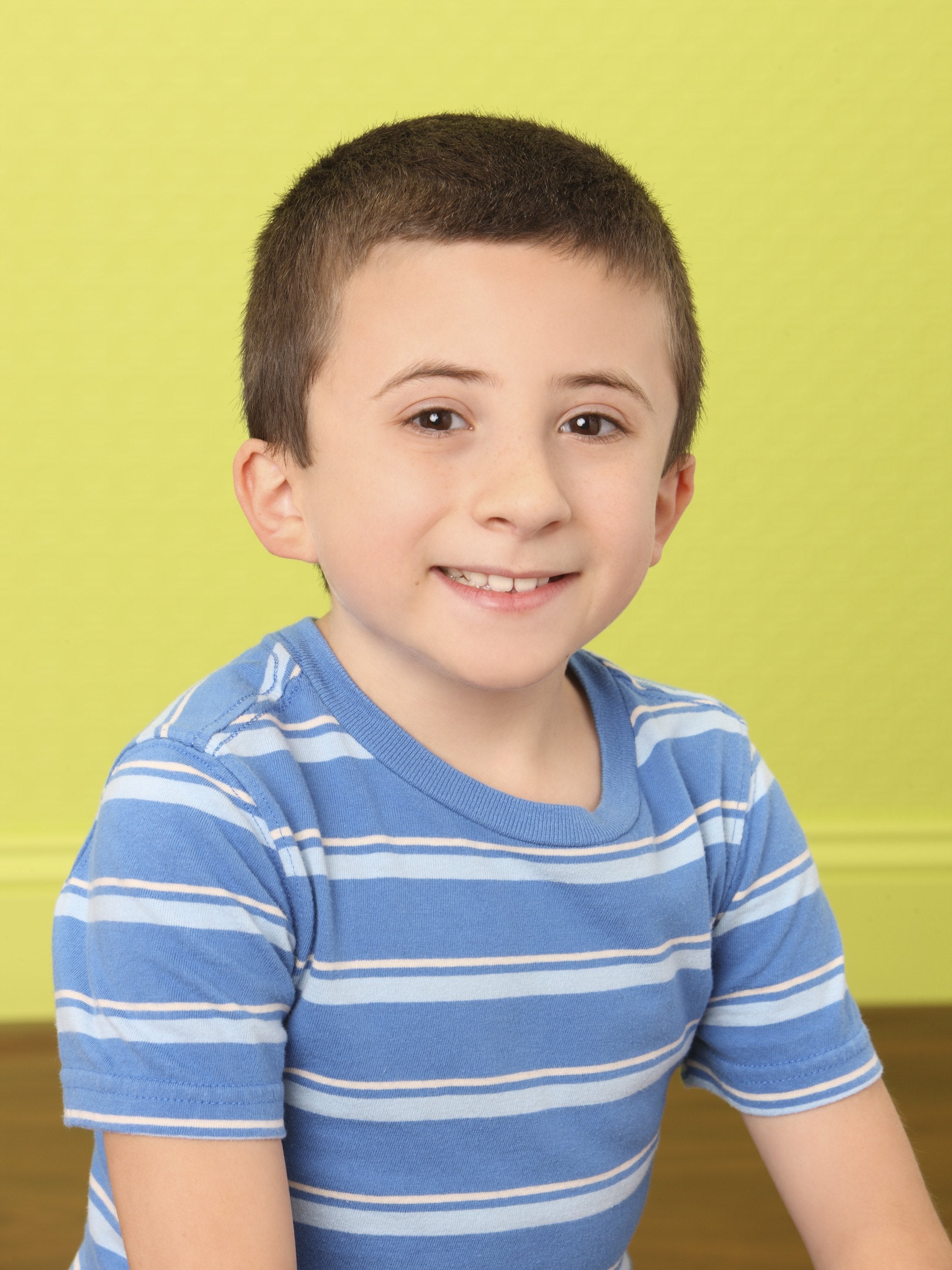 A young child smiling, wearing a striped shirt, against a simple background