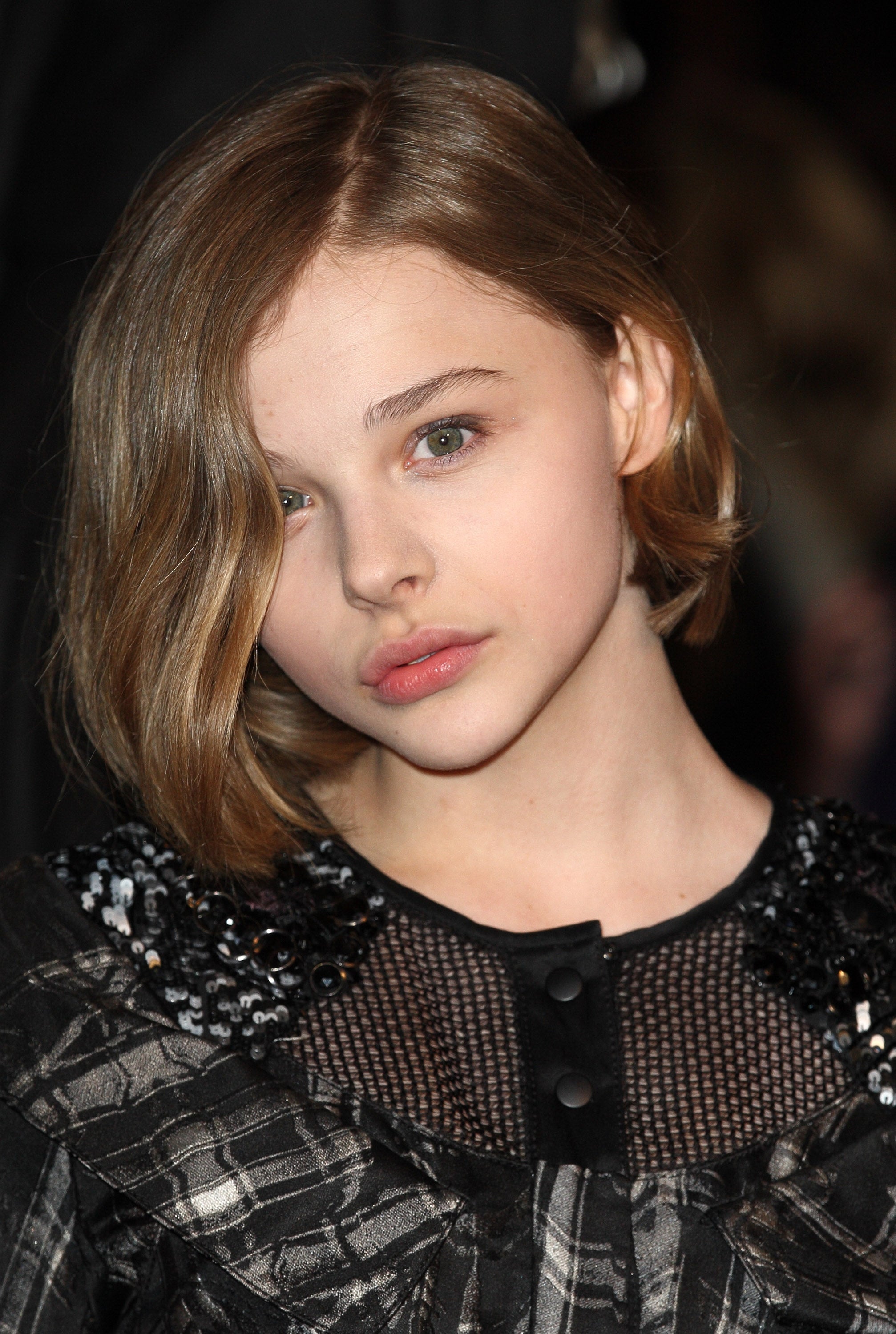 A person with shoulder-length hair poses in a patterned dress with mesh and sequin details