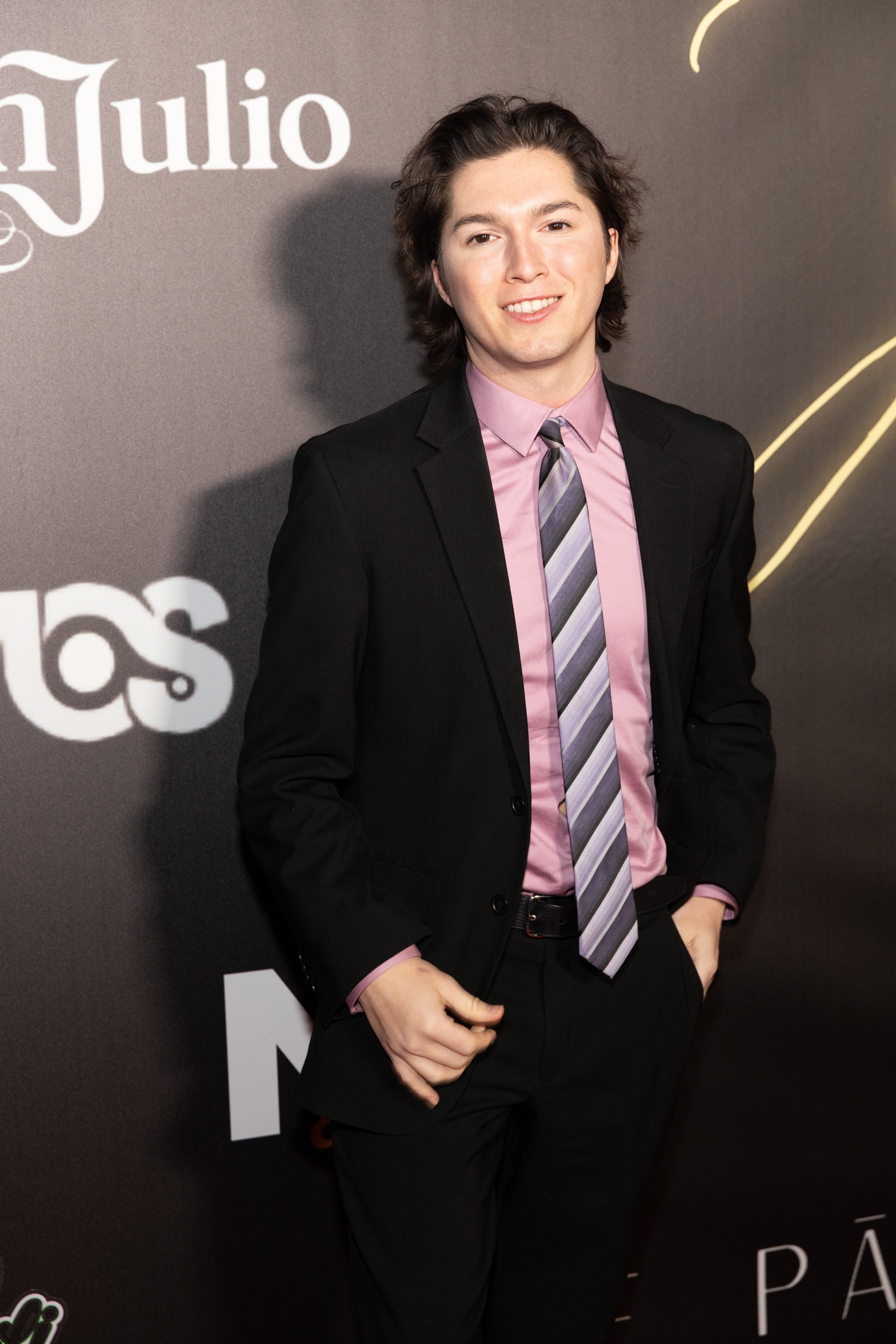 Person in a suit with a patterned tie poses confidently on a media event backdrop