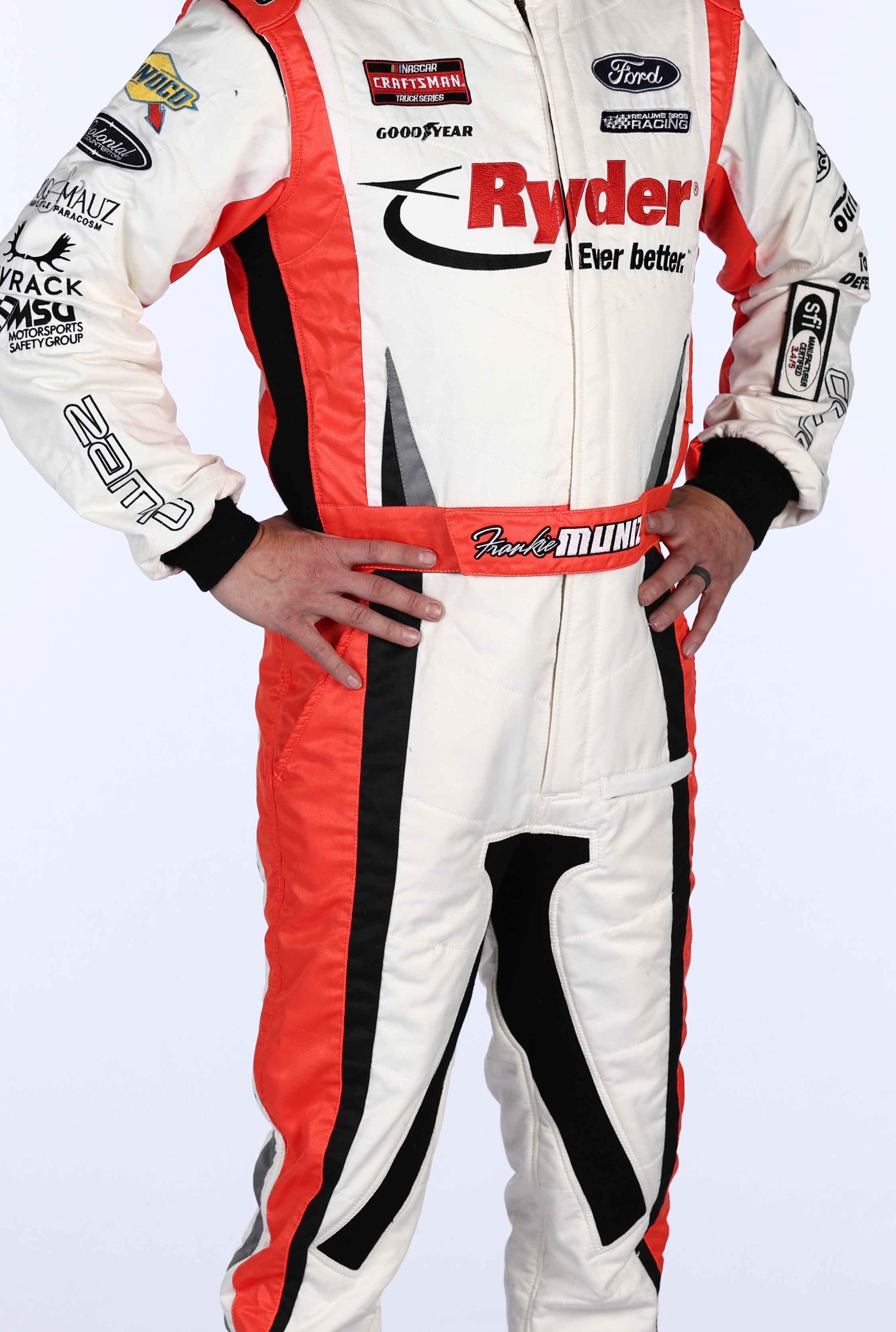 Person in a racing suit with sponsor logos, standing confidently with hands on hips, looking forward