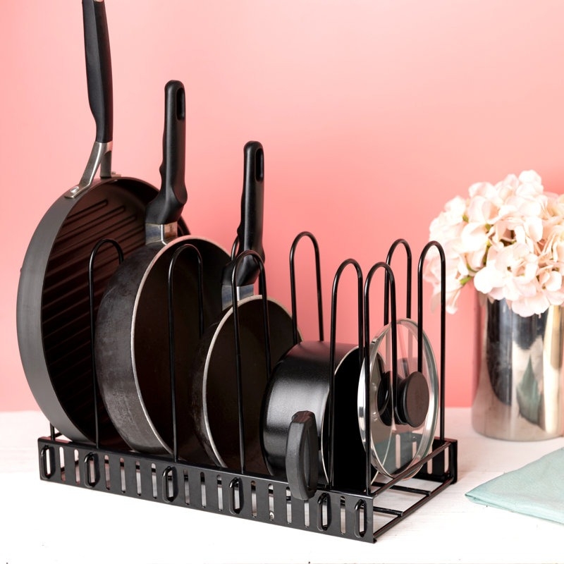 Cookware organizer with various pots and pans neatly arranged, set against a backdrop with flowers and a soft pink wall