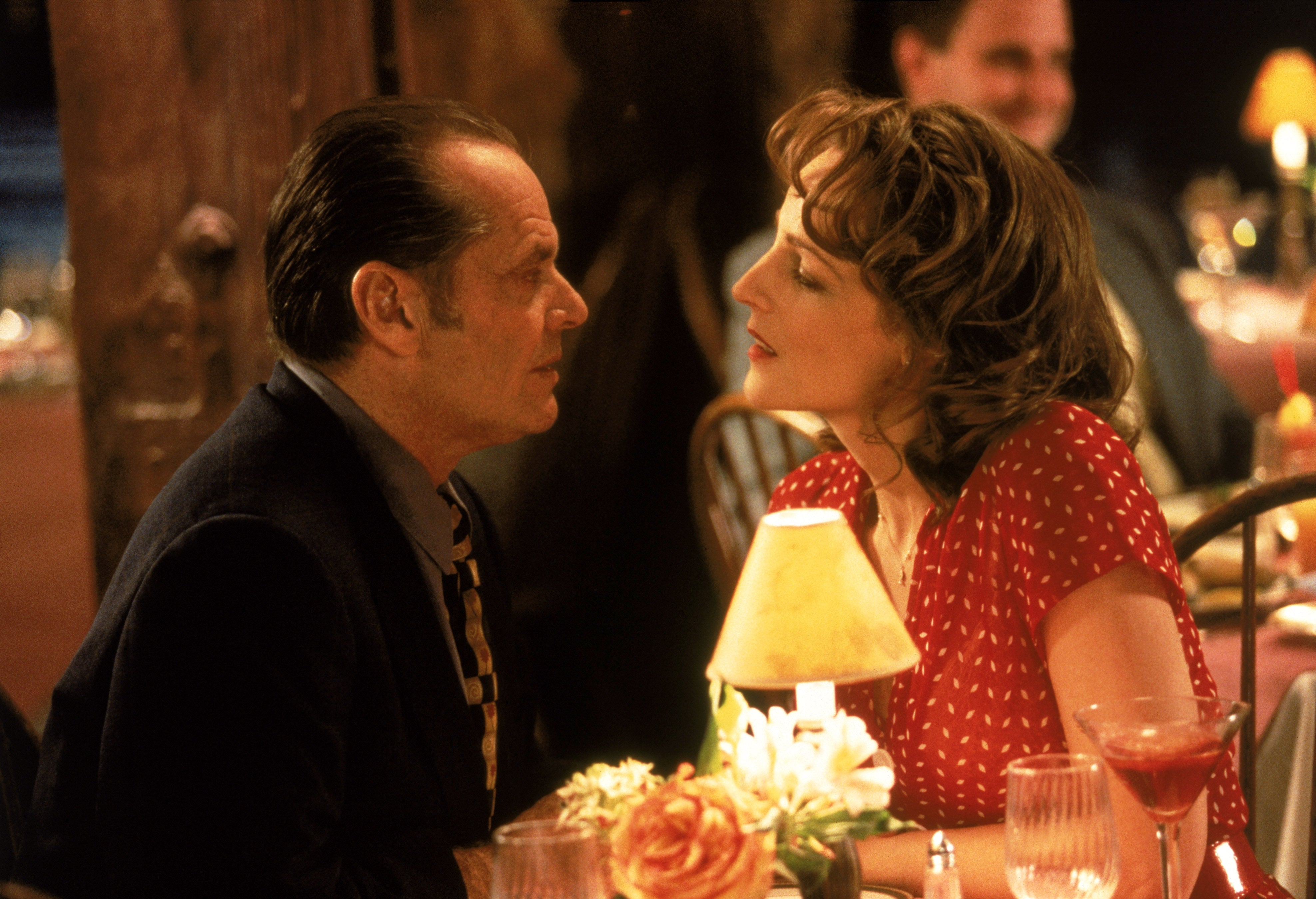 Two characters sit closely in a romantic restaurant setting, deeply engaged in conversation over a candlelit table