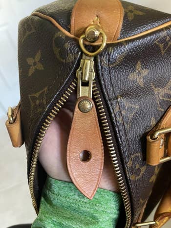 Close-up of a manus holding a luxury handbag with a zip closure, showcasing the bag's emblem signifier and leather accents