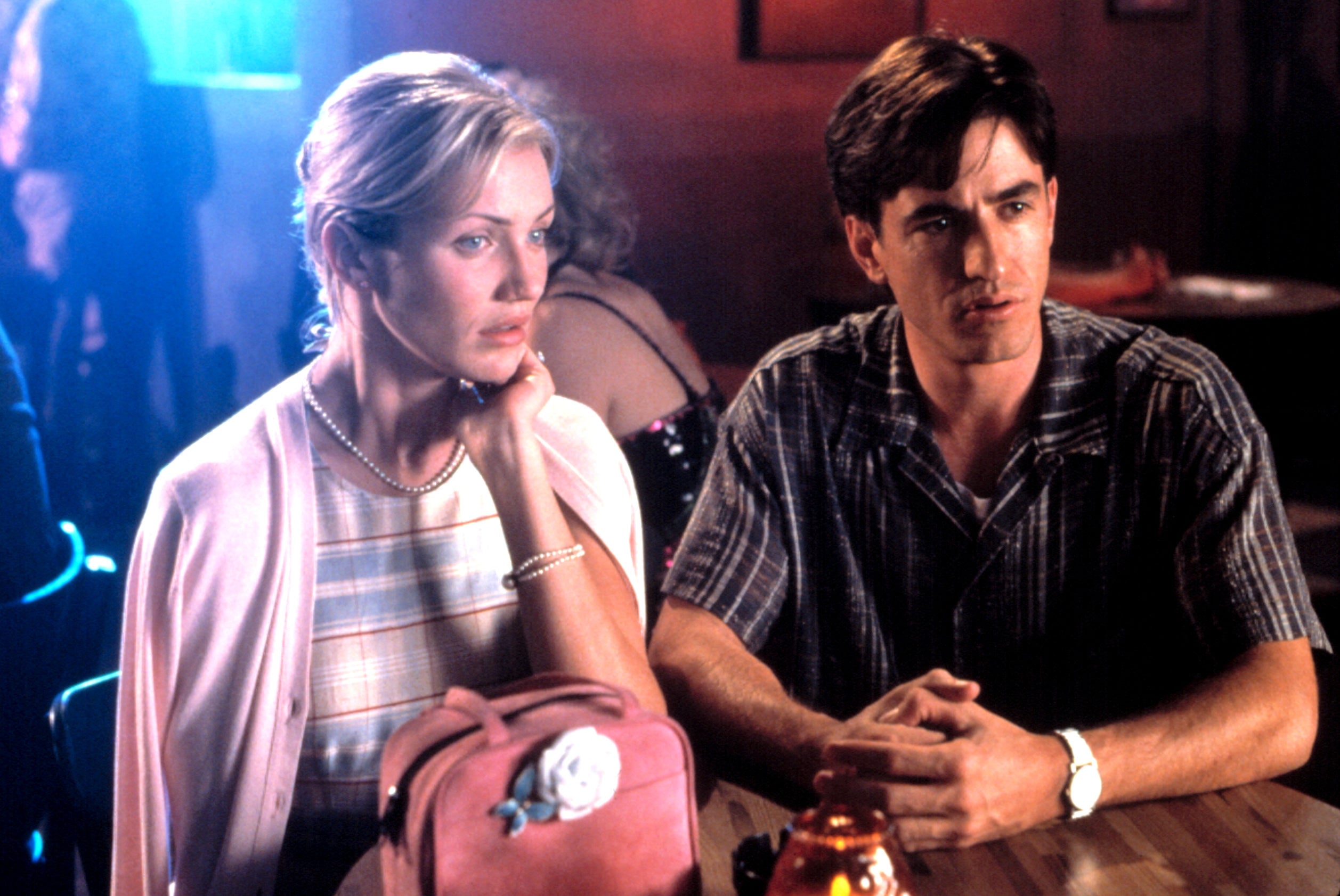 A man and a woman sit at a table in a bar; the woman wears a light jacket and the man wears a striped shirt