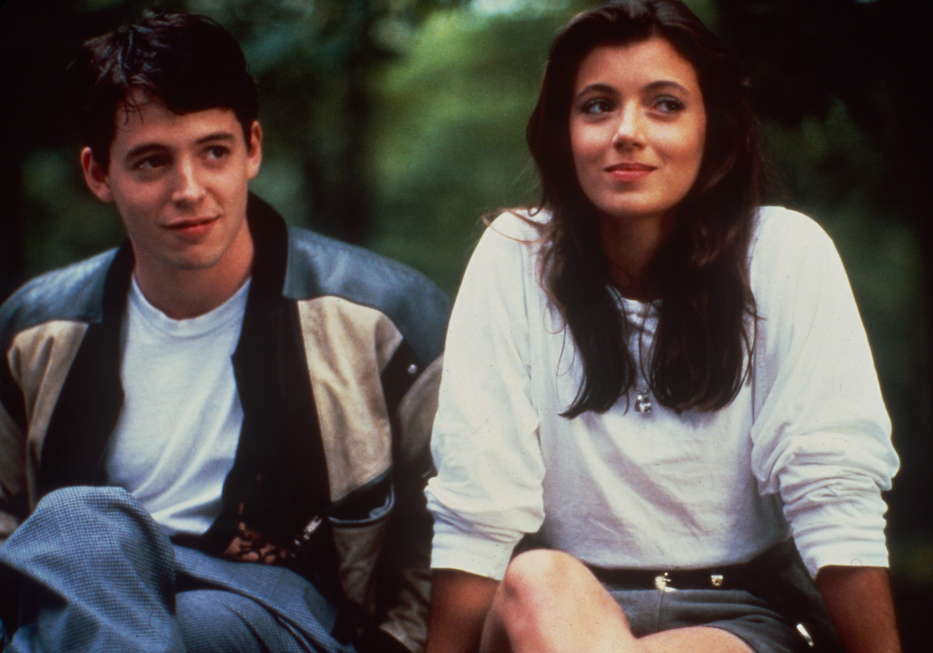 A man in a casual jacket smiles beside a woman in a simple top, both seated outdoors