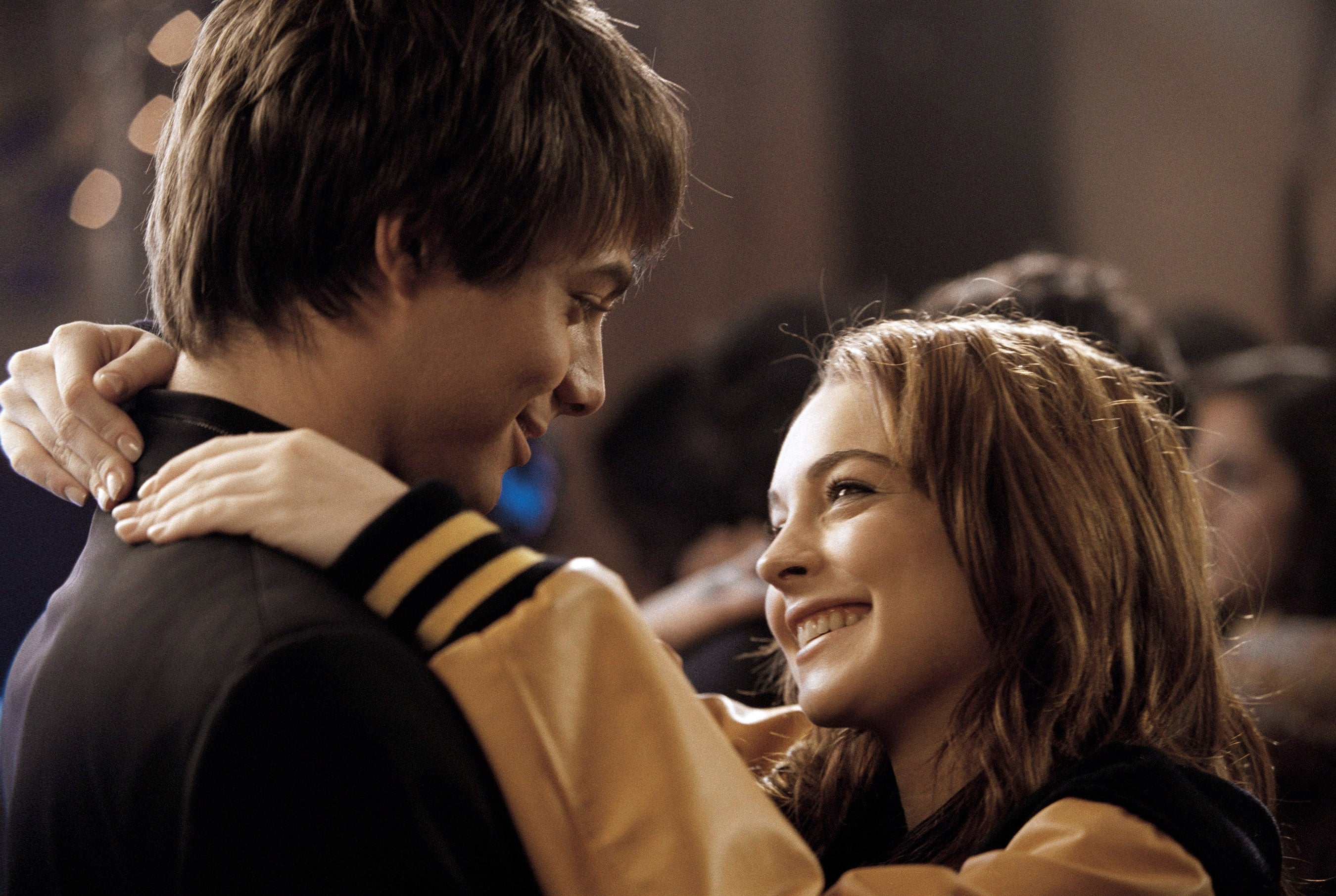 Two people smile at each other while dancing closely, their arms around each other's shoulders, creating a warm, romantic atmosphere