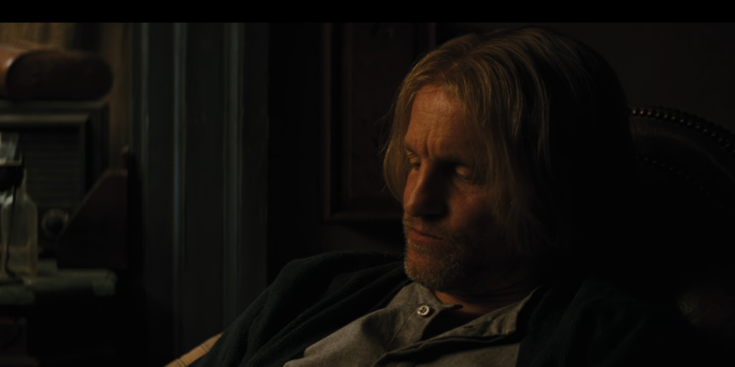 Haymitch sitting pensively in a dimly lit room in a movie scene