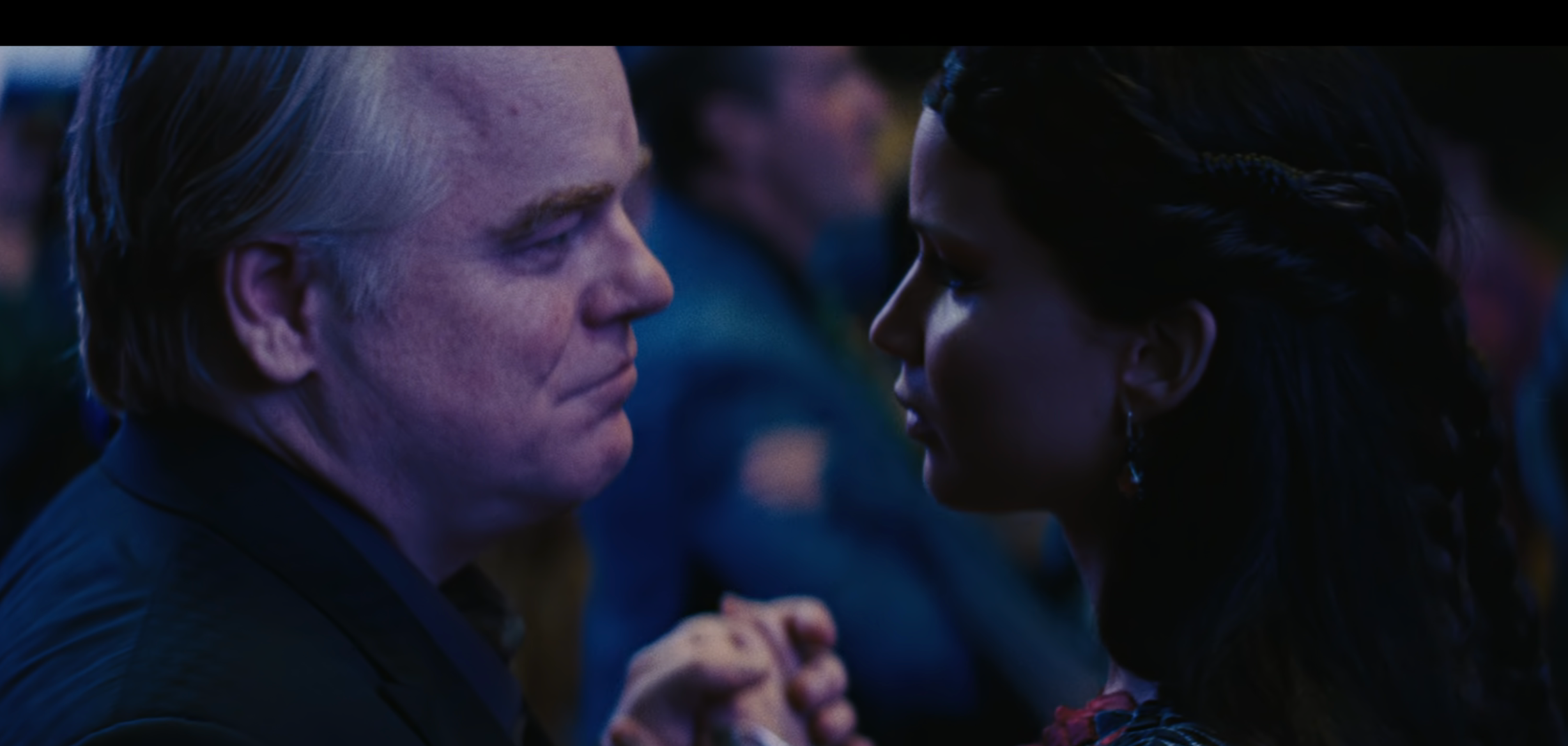 Phillip Seymour Hoffman as Plutarch, dancing with Katniss at a formal event in a movie scene