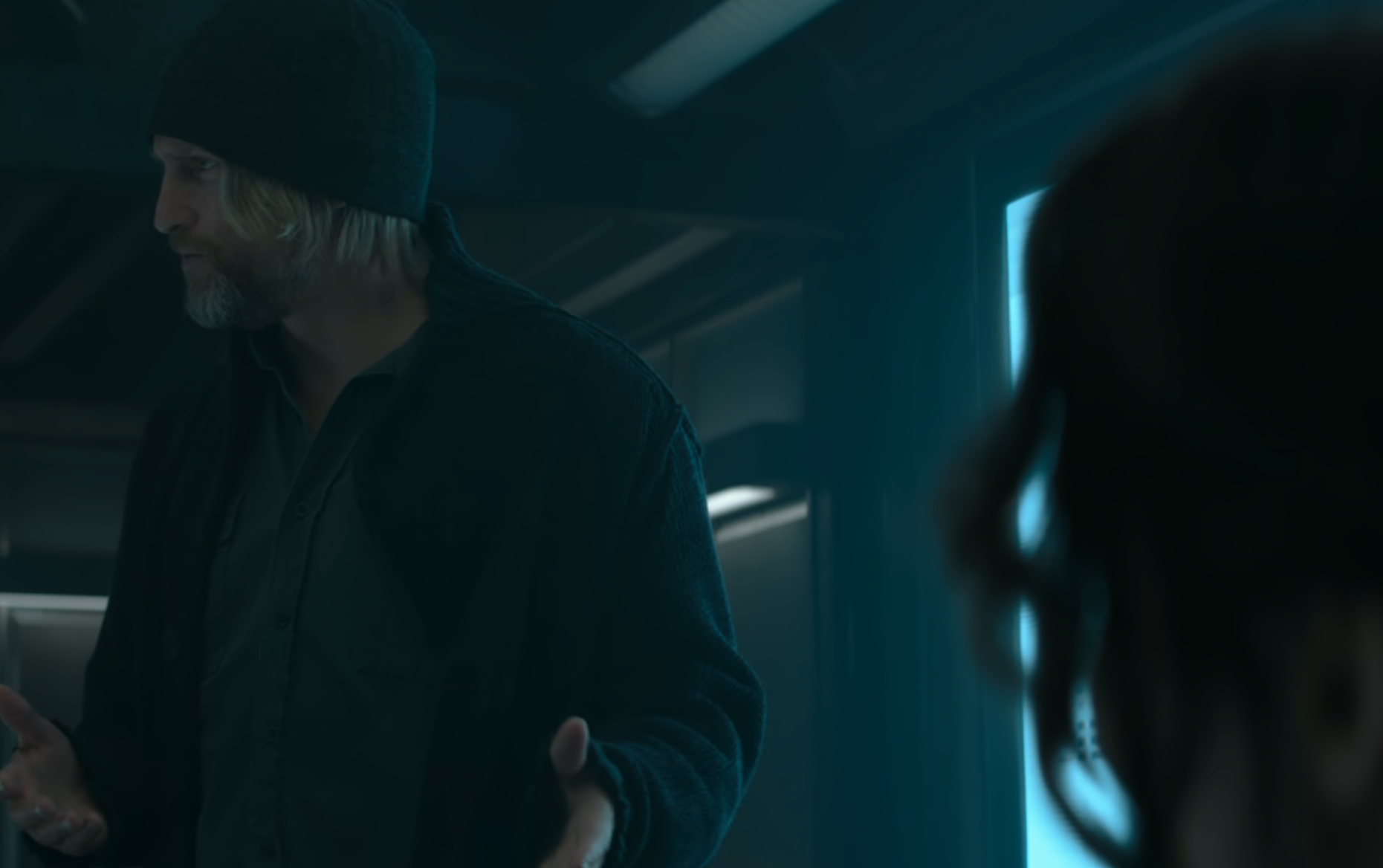 Haymitch wearing a beanie and jacket, talking to another person in a movie scene
