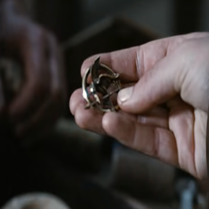 A hand holds a small mockingjay pin