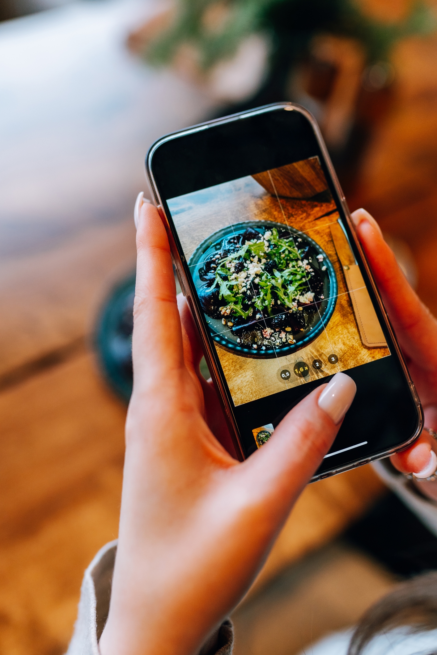 Person som fotograferer en skål med salat med en smarttelefon, med fokus på detaljer som greener og pålegg