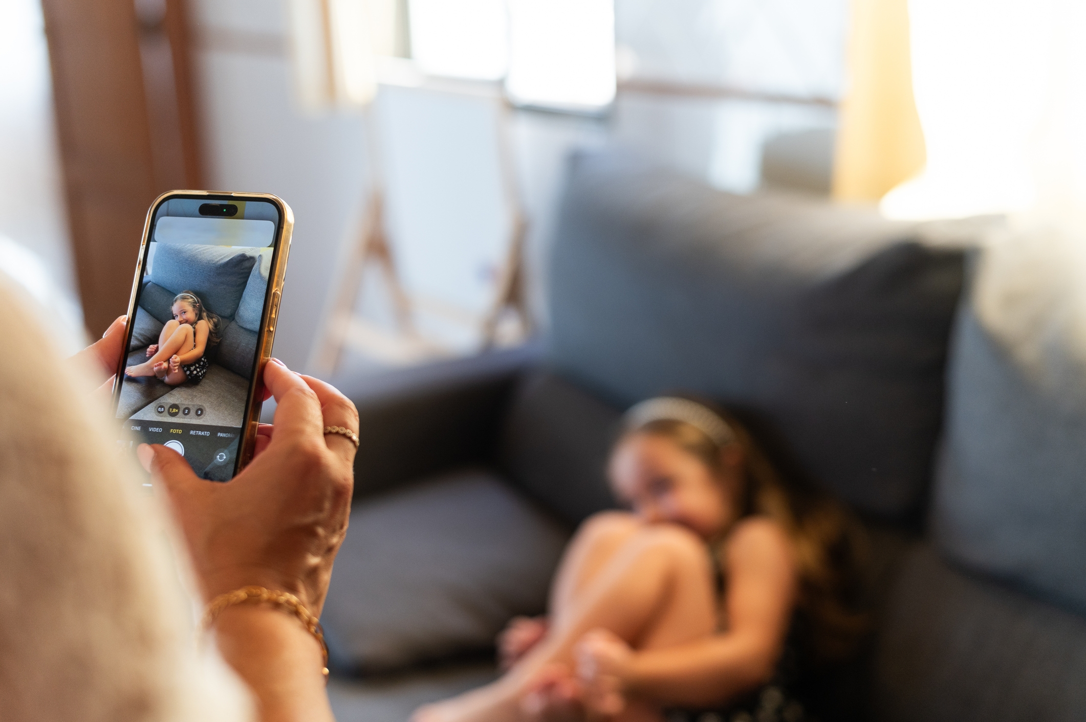 Person som fotograferer et barn som er krøllet sammen på en sofa ved hjelp av en smarttelefon, og fanger et øyeblikk av hvile eller ettertanke