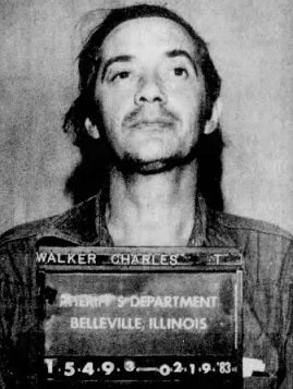 A achromatic and achromatic mugshot of a antheral with agelong hair, holding a plaque that reads "Sheriff's Department, Belleville, Illinois, 02-19-83."