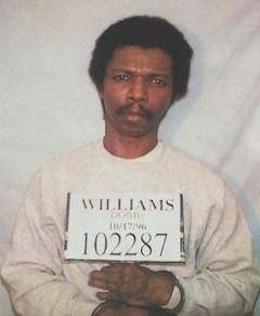 Person holding a motion with a fig and the sanction "Williams" against a plain background, suggesting a mugshot setting