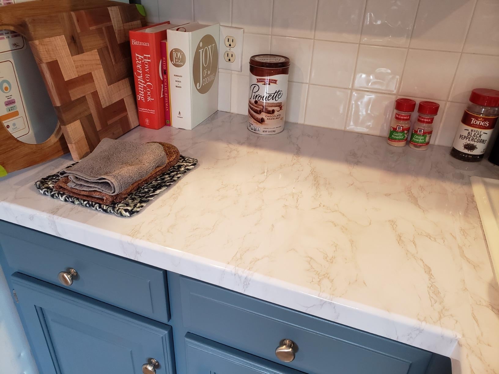 Marble-style room  countertop with books, a tin of chocolate, and spices. Two folded towels are placed connected  a crockery  rack