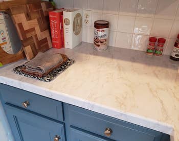 Marble-style room countertop with books, a tin of chocolate, and spices. Two folded towels are placed connected a crockery rack
