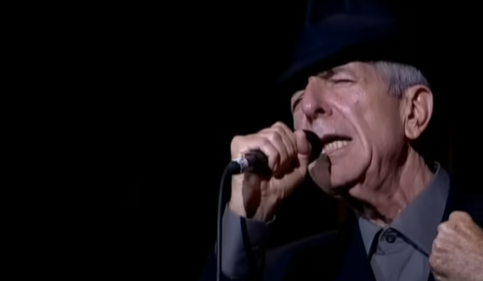 Singer wearing a suit and hat performs passionately on stage, gripping a microphone close