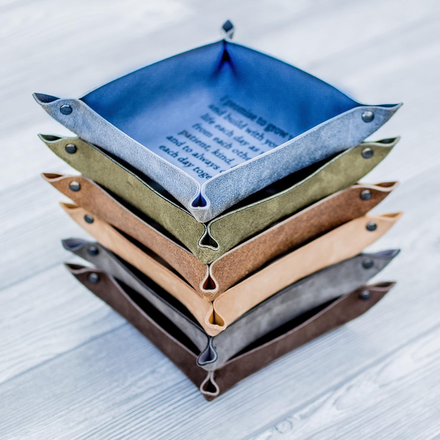 Stack of five leather valet trays on a wooden surface, each in a different neutral tone, showcasing organized storage for personal items