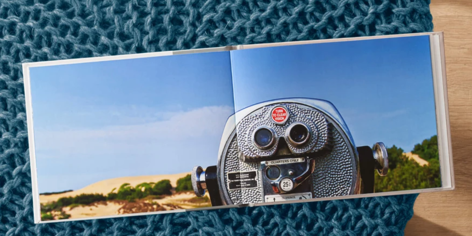 A photo book open to a page showing a viewfinder overlooking a sandy landscape; placed on a woven surface