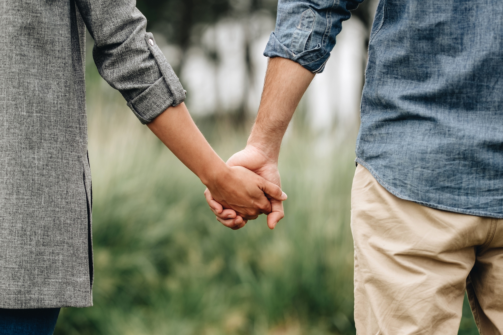 To personer holder hendene utendørs, den ene i en langermet skjorte, den andre i en denimskjorte og beige bukser, symboliserer forbindelse og støtte