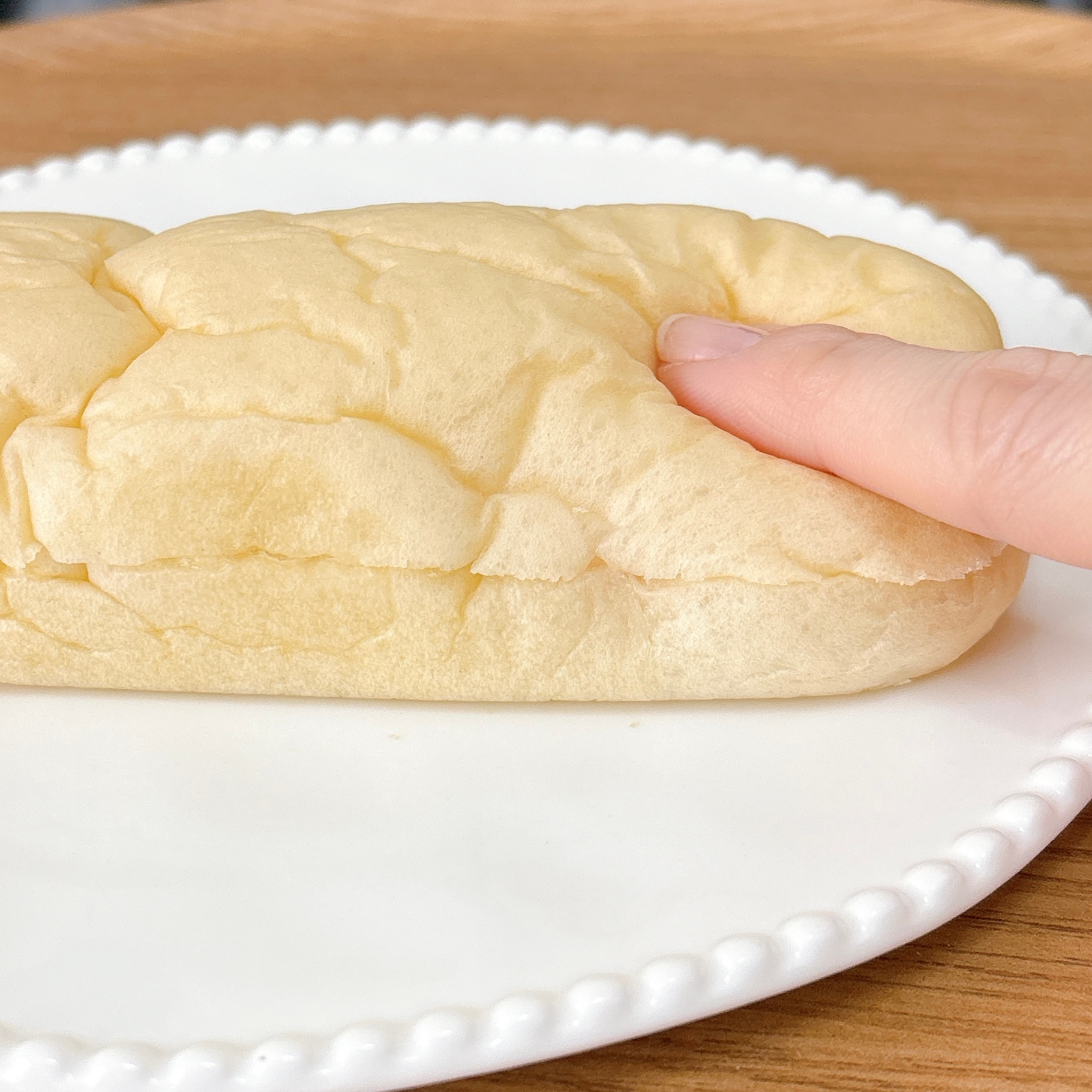 白い皿にふんわりとしたロールパンが置かれ、指で軽く押されている様子。