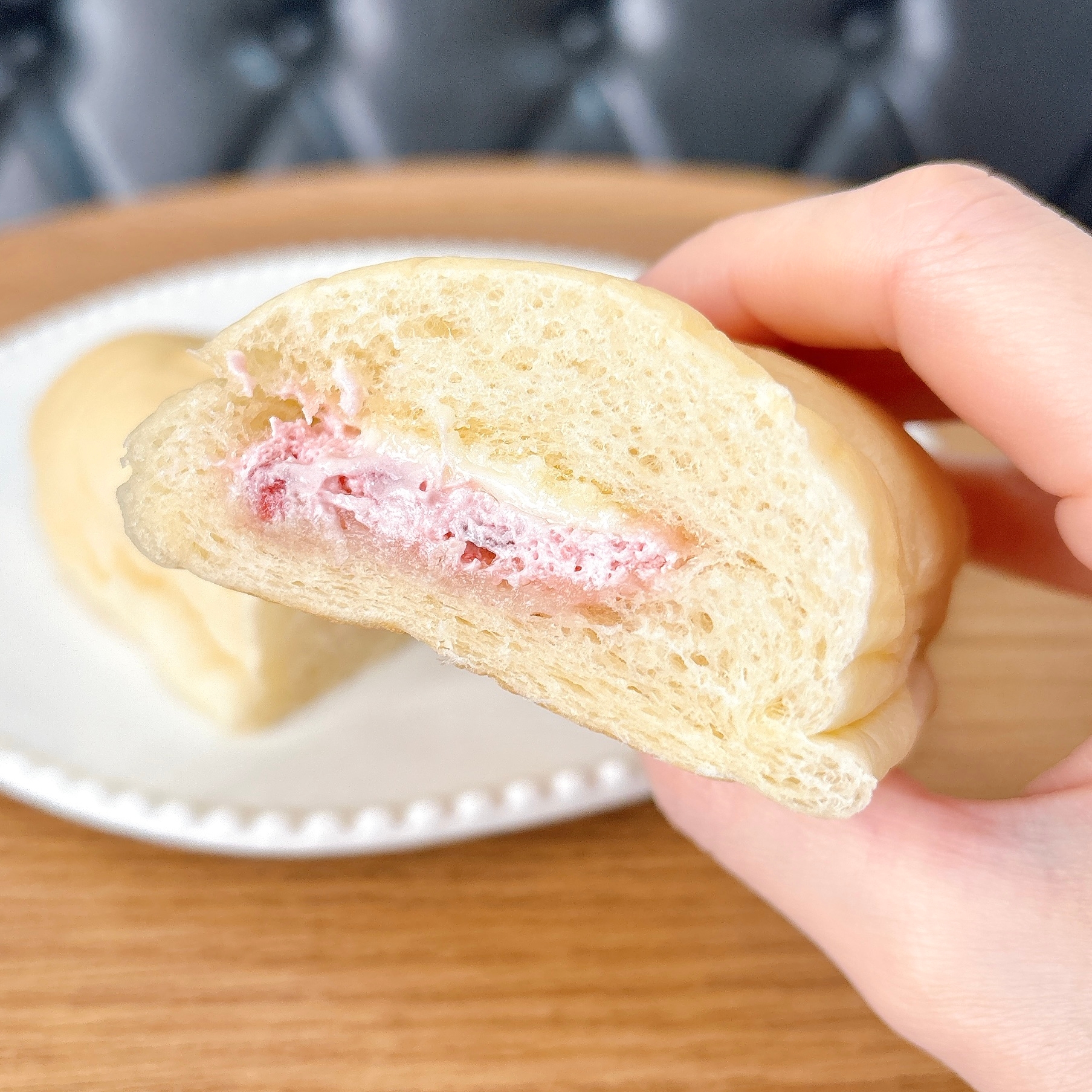 手に持った半分にカットされたパン。イチゴクリームが入っている。背景に他のパンが皿に載っている。