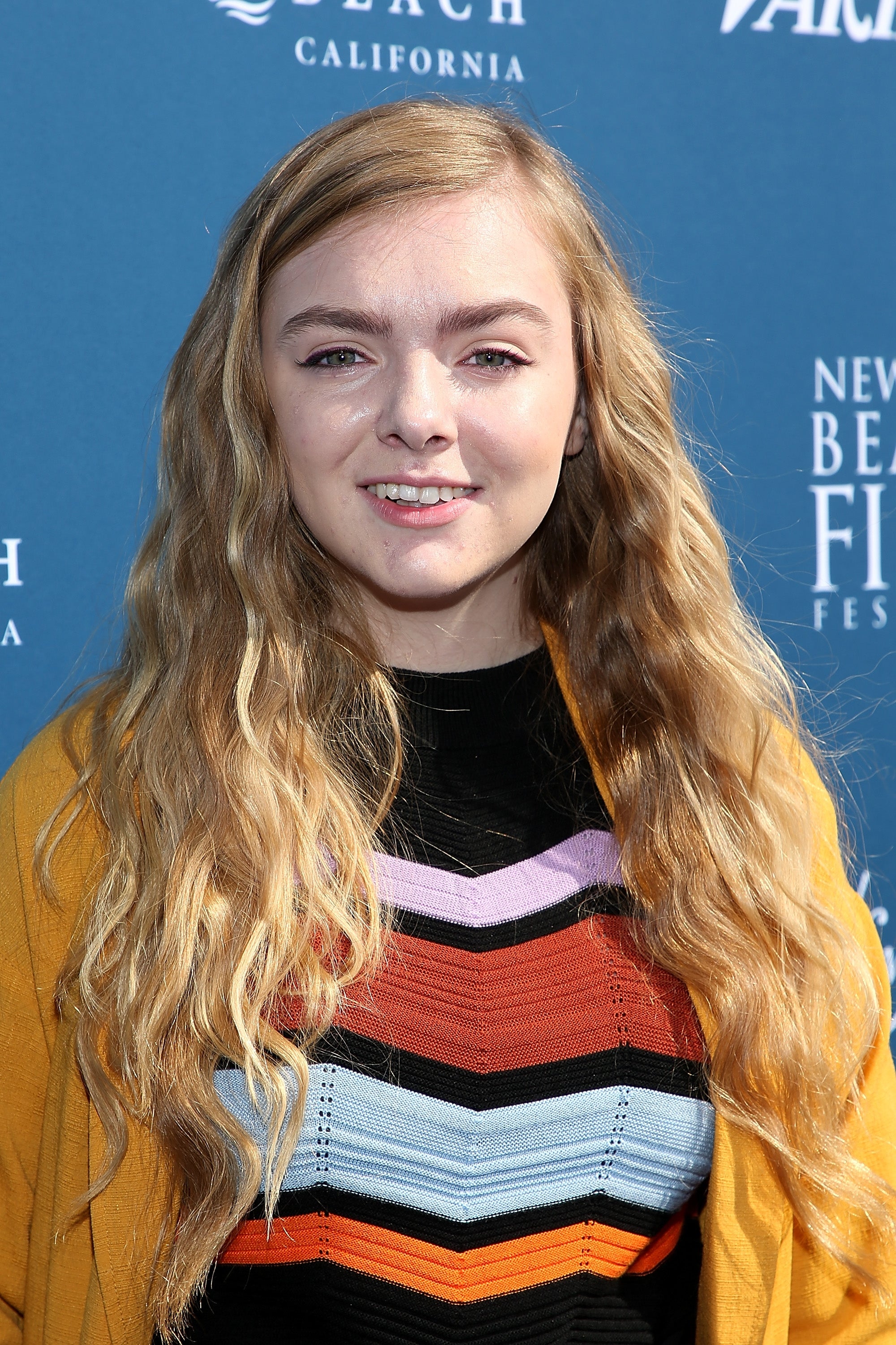 Person with long wavy hair at a film festival, wearing a striped top and cardigan, in front of a backdrop with festival text