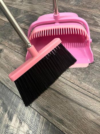 Pink broom and dustpan acceptable connected a woody floor, showcasing cleaning tools for location use
