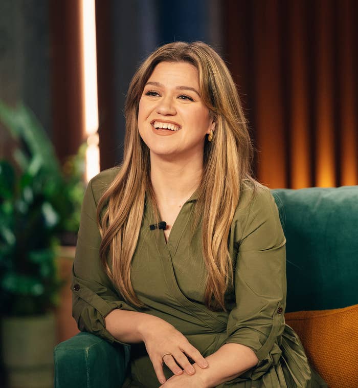 Kelly Clarkson smiling while sitting on a green armchair